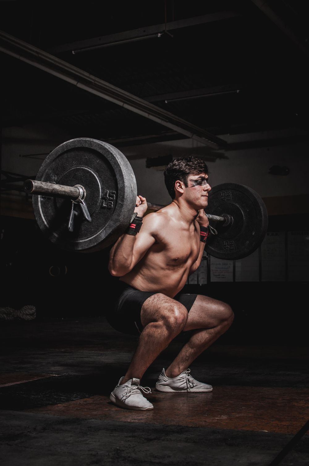 Coach Dominic Reyes holding a front-loaded squat under a bar in a blacked-out hall