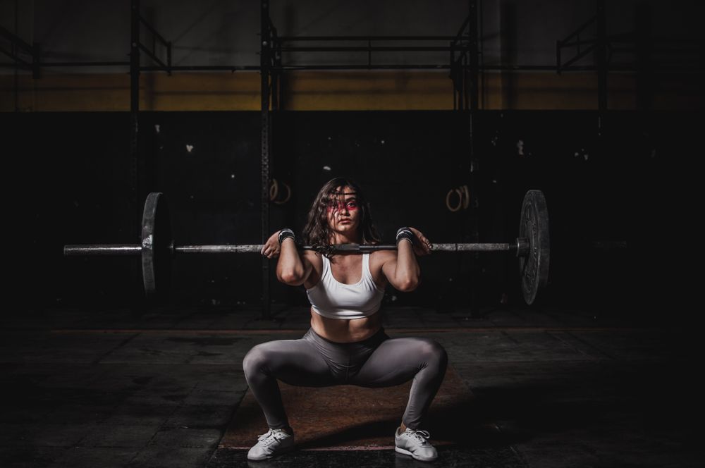 Coach Mara Okafor in a deep front squat with a loaded barbell, low key lighting