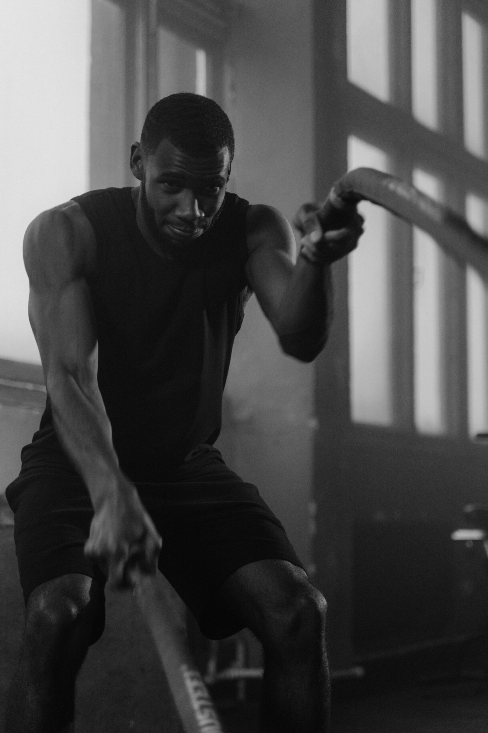 Athlete pulling on a rowing machine under hard overhead light, sweat on the forearms