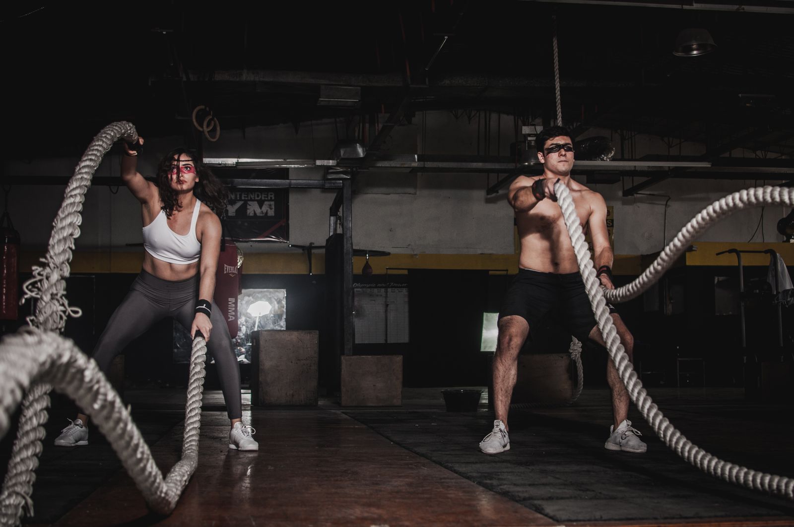 Two members driving heavy battle ropes on a dark conditioning floor